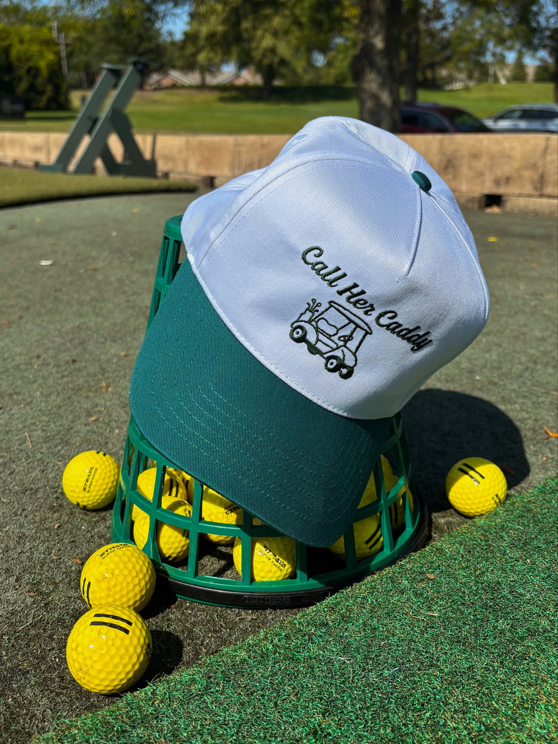 Golf hat with 'Call Her Caddy' text and design on a grassy area with golf balls and a basket.