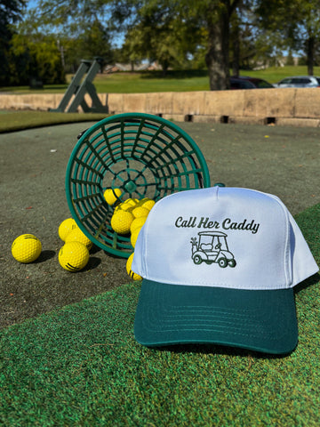 Golf hat with 'Call Her Caddy' text and design on a grassy area with golf balls and a basket.