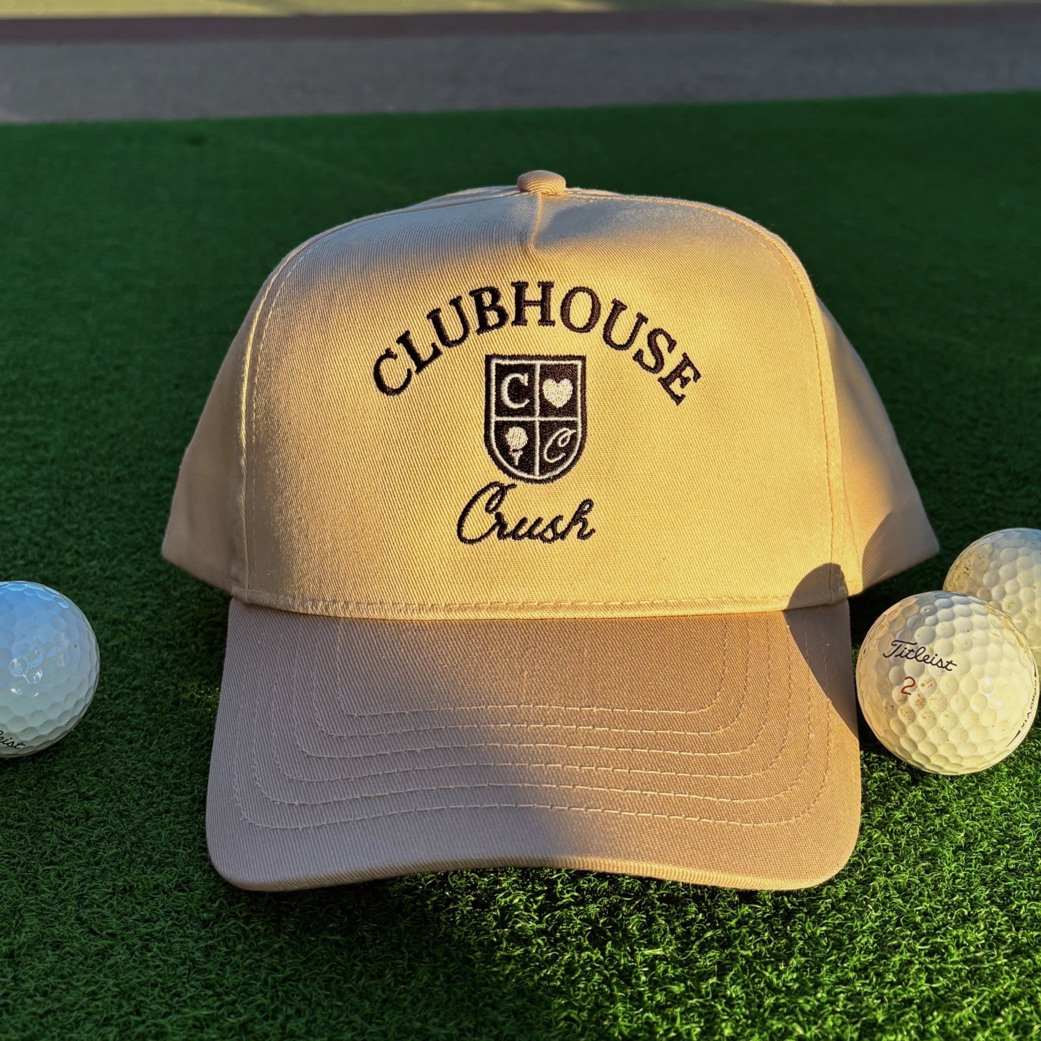 Beige cap with 'Clubhouse Crush' logo on a green surface with golf balls.