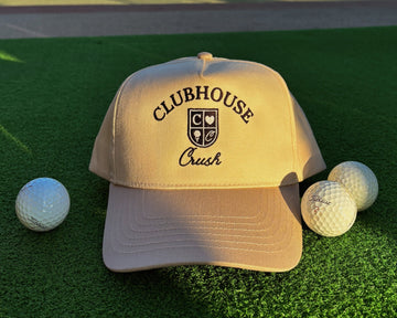 Beige cap with 'Clubhouse Crush' logo on a green surface with golf balls.